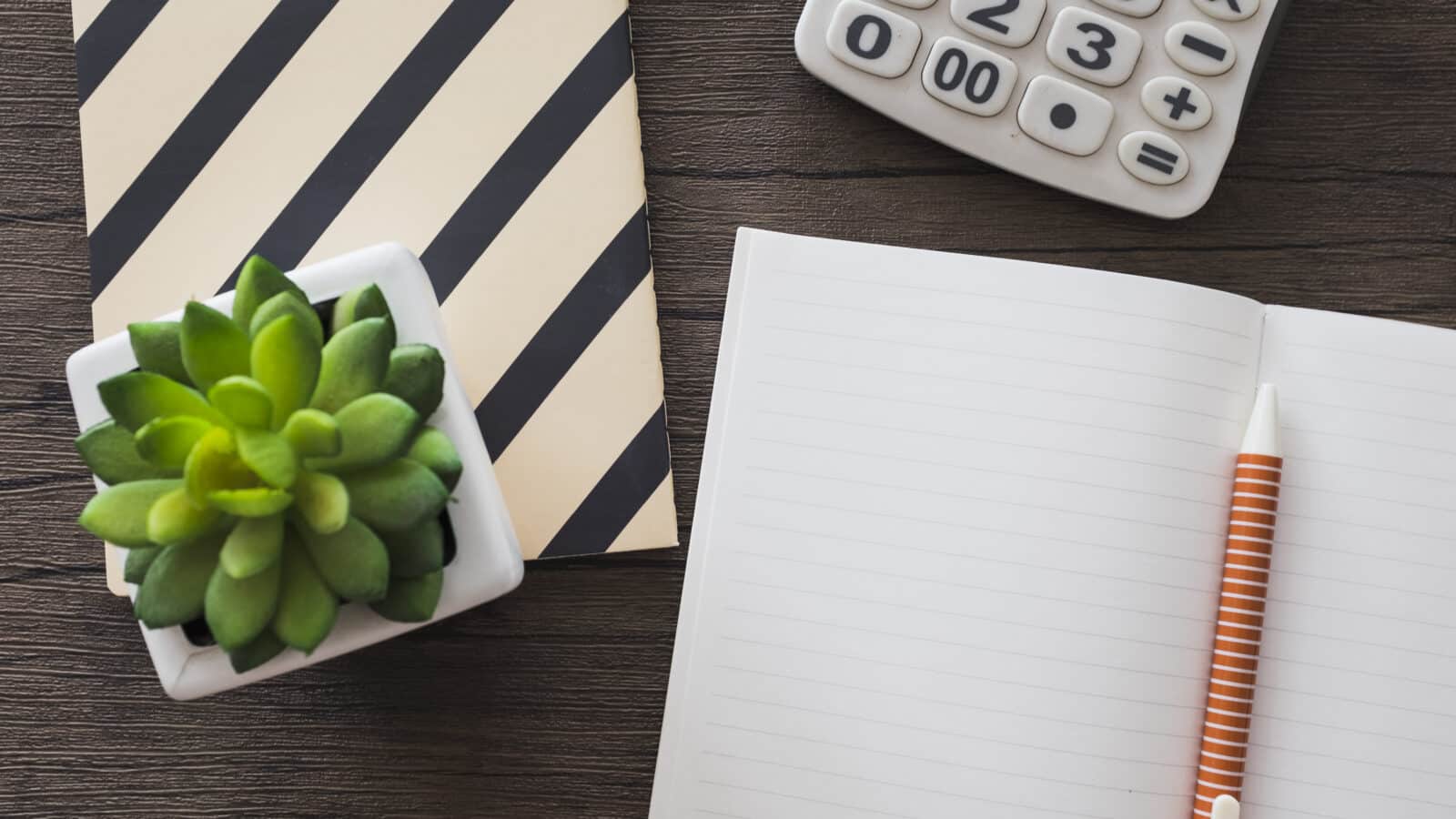 Calculatrice, carnet et stylo sur un bureau en bois, vue de dessus, comptabilité d'une location meublée