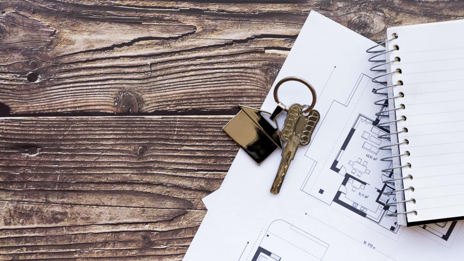 Clés de logement posées sur un plan et un carnet, bureau en bois