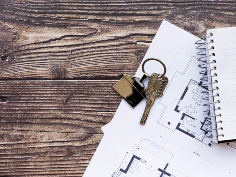 Clés de logement posées sur un plan et un carnet, bureau en bois