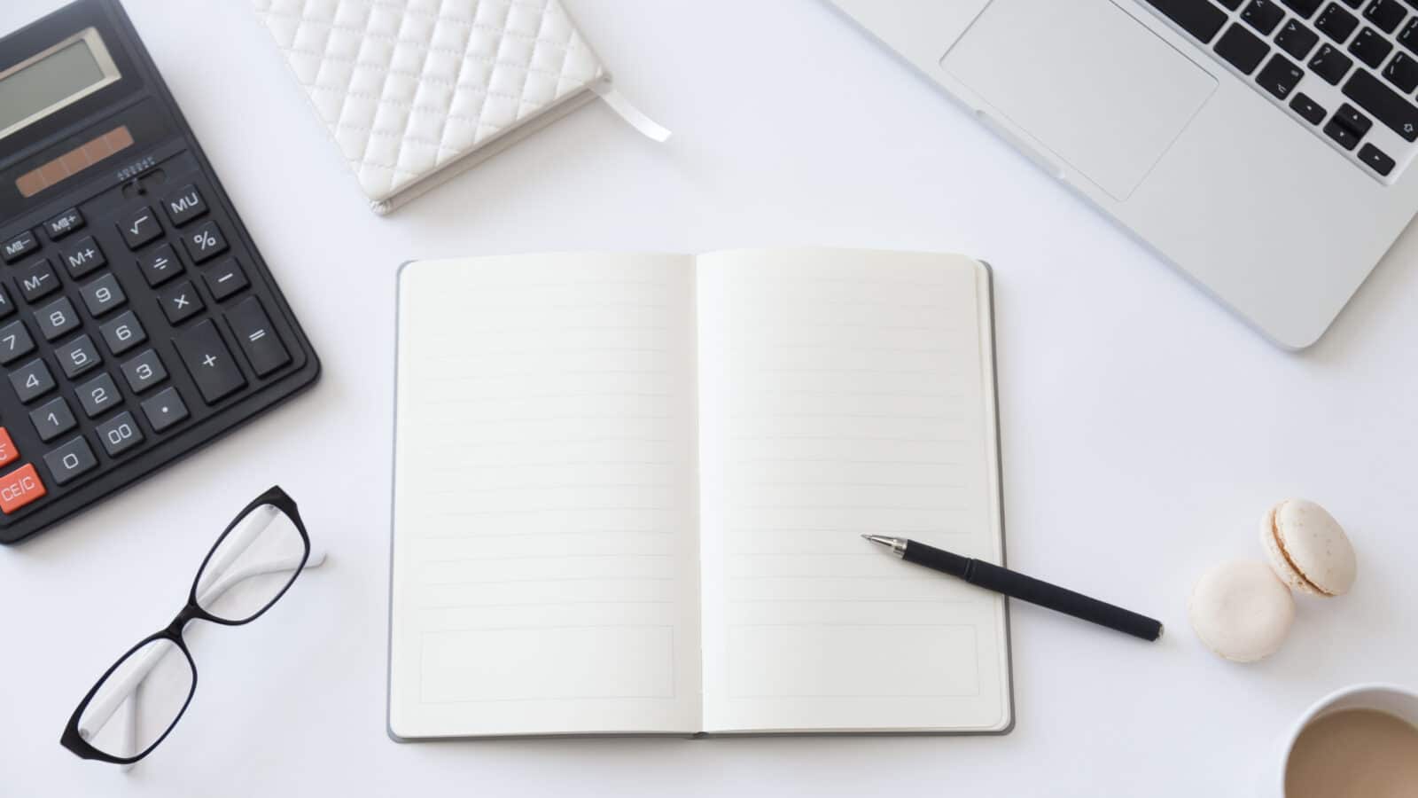 Bureau vu de dessus avec carnet ouvert et stylo, tenue de la comptabilité d'une location meublée soi-même