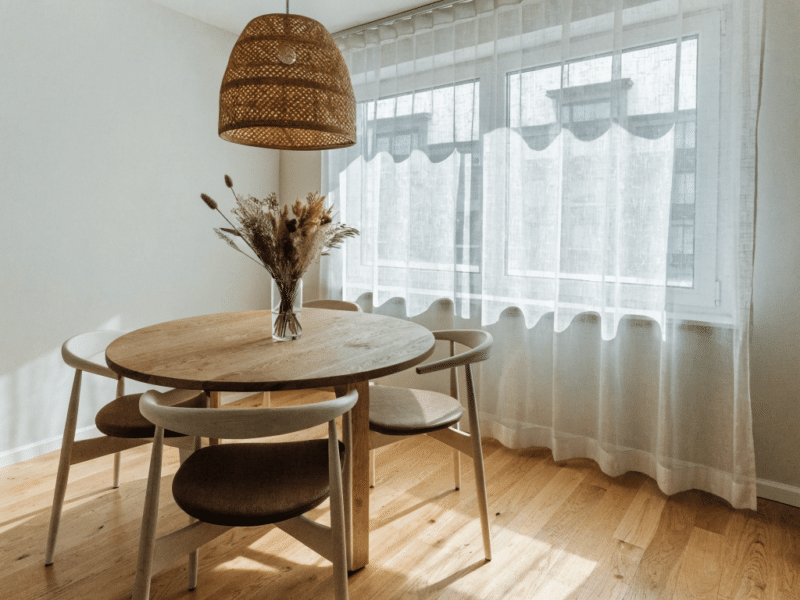 Coin repas lumineux avec table ronde en bois clair et suspension en rotin