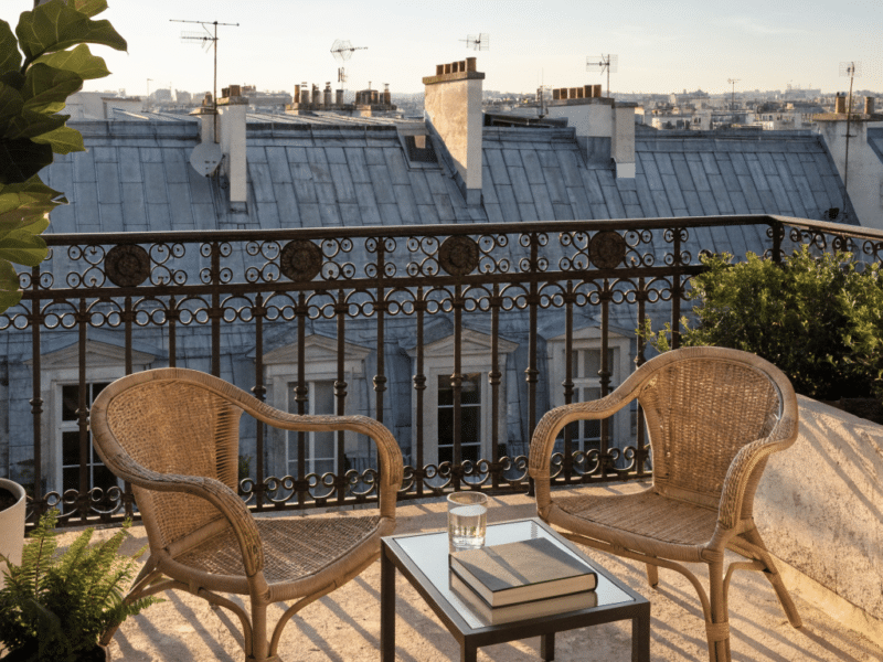 Balcon parisien avec fauteuils en rotin et vue sur les toits en zinc